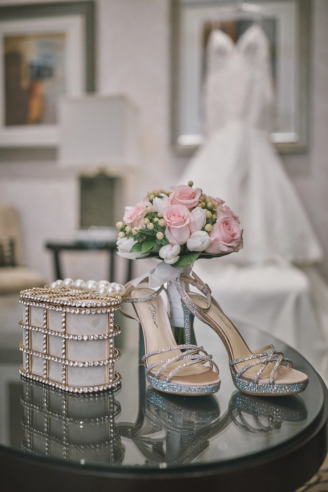 Bridal bouquet, crystal shoes, and evening bag arranged before a wedding dress