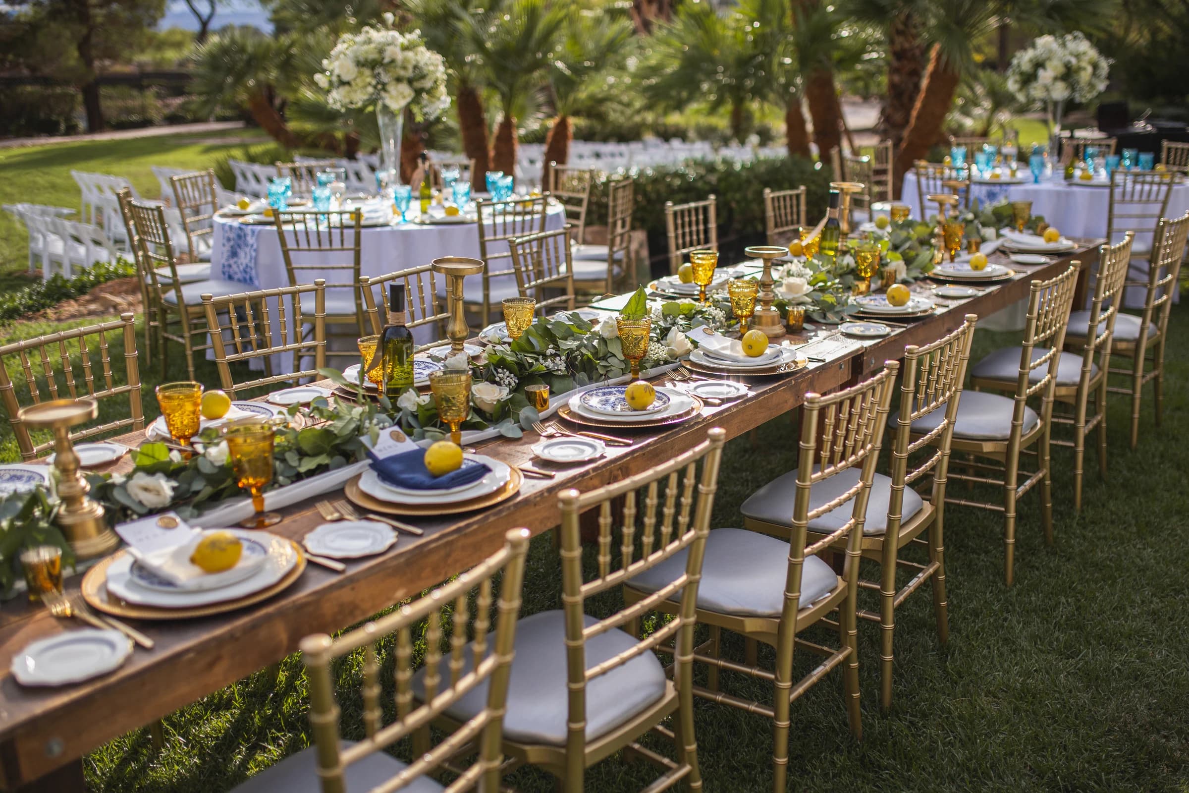 Outdoor wedding reception tables set with gold chairs, flowers, and colorful glassware